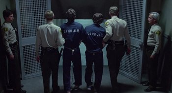 Movie still from “The Falcon and the Snowman” (1985), directed by John Schlesinger – A group of men standing next to each other in a room; Wide shot, Low angle