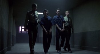 Movie still from “The Falcon and the Snowman” (1985), directed by John Schlesinger – A group of men standing next to each other in a room; Wide shot, Low angle