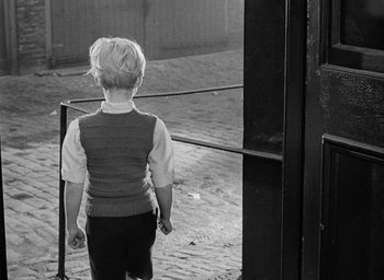 Movie still from “The Fallen Idol” (1948), directed by Carol Reed – A little boy standing in front of an open gate; Medium shot, Over the shoulder angle