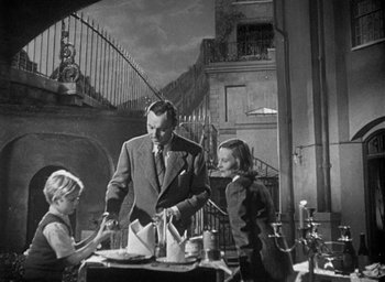Movie still from “The Fallen Idol” (1948), directed by Carol Reed – An old photo of a man and two children at a table; Medium shot, High angle