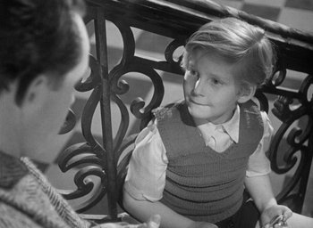 Movie still from “The Fallen Idol” (1948), directed by Carol Reed – A young boy sitting next to an older woman; Medium shot, Over the shoulder angle