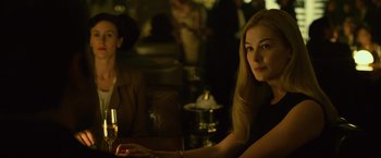 Movie still from “Gone Girl” (2014), directed by David Fincher – A woman sitting at a table with a glass of wine in front of her; Medium shot, Over the shoulder angle