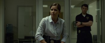 Movie still from “Gone Girl” (2014), directed by David Fincher – A woman in a police uniform is standing in front of a door; Medium shot, Over the shoulder angle