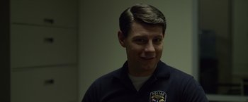 Movie still from “Gone Girl” (2014), directed by David Fincher – A man in a police uniform smiling for the camera; Close Up shot, Over the shoulder angle