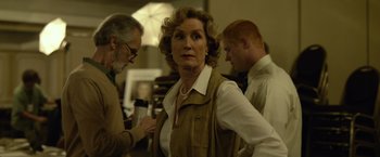 Movie still from “Gone Girl” (2014), directed by David Fincher – An older woman in a brown vest is looking at the camera while two other people look on; Medium shot, Over the shoulder angle