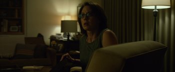 Movie still from “Gone Girl” (2014), directed by David Fincher – A woman sitting in a chair in front of a television; Medium shot, Over the shoulder angle