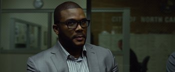 Movie still from “Gone Girl” (2014), directed by David Fincher – A person wearing a suit and glasses; Close Up shot, Over the shoulder angle