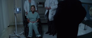 Movie still from “Gone Girl” (2014), directed by David Fincher – A woman sitting in a chair in a room with other doctors; Medium shot, Over the shoulder angle