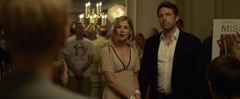 Movie still from “Gone Girl” (2014), directed by David Fincher – A woman standing next to a man in front of a crowd; Medium shot, Over the shoulder angle