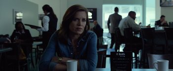 Movie still from “Gone Girl” (2014), directed by David Fincher – A woman sitting at a table with a cup of coffee in front of her; Medium shot, Over the shoulder angle