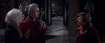 Movie still from “The Fearless Vampire Killers” (1967), directed by Roman Polanski – An older man smoking a pipe while wearing a red jacket; Medium shot, Over the shoulder angle