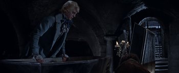 Movie still from “The Fearless Vampire Killers” (1967), directed by Roman Polanski – A man standing in a dark room next to a fire pit; Wide shot, Low angle