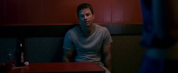 Movie still from “The Fighter” (2010), directed by David O. Russell – A man sitting at a table in front of a red wall; Medium shot, Low angle