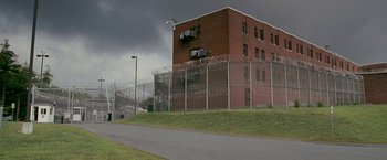 Movie still from “The Fighter” (2010), directed by David O. Russell – A building that is next to a chain link fence; Extreme Wide shot, Low angle