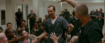 Movie still from “The Fighter” (2010), directed by David O. Russell – A group of people in a room with a man in a black shirt; Medium shot, Over the shoulder angle