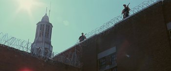 Movie still from “The Fighter” (2010), directed by David O. Russell – A man standing on top of a building near a barbed - wire fence; Extreme Wide shot, Low angle