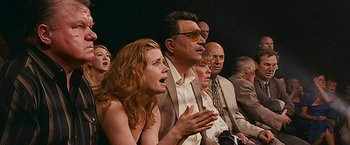 Movie still from “The Fighter” (2010), directed by David O. Russell – A group of people sitting next to each other on a stage; Medium shot, Low angle