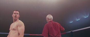 Movie still from “The Fighter” (2010), directed by David O. Russell – An older man wearing a red shirt is in a boxing ring; Medium shot, High angle