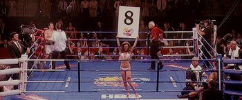 Movie still from “The Fighter” (2010), directed by David O. Russell – A woman in a bikini holds up a sign in a boxing ring; Medium shot, High angle