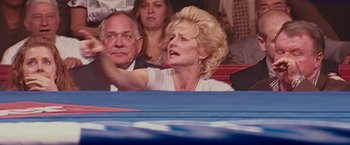Movie still from “The Fighter” (2010), directed by David O. Russell – An older woman in a white shirt is in a crowd; Medium shot, High angle