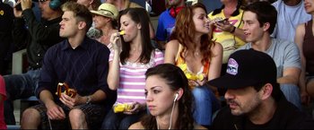 Movie still from “The Final Destination” (2009), directed by David R. Ellis – A group of people sitting in a stadium eating bananas; Medium shot, Over the shoulder angle