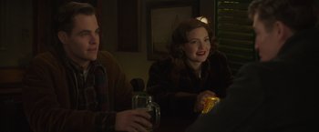 Movie still from “The Finest Hours” (2016), directed by Craig Gillespie – A woman sitting at a table with a glass of beer; Medium shot, Over the shoulder angle