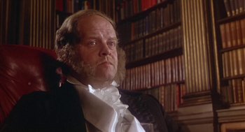 Movie still from “The Great Train Robbery” (1978), directed by Michael Crichton – A man in a suit and tie in front of a book shelf; Close Up shot, Low angle