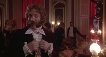 Movie still from “The Great Train Robbery” (1978), directed by Michael Crichton – A man with a long beard and a bow tie in front of a group of people; Medium shot, Low angle