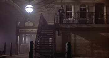 Movie still from “The Great Train Robbery” (1978), directed by Michael Crichton – A man standing on top of a set of stairs next to a building; Wide shot, Low angle
