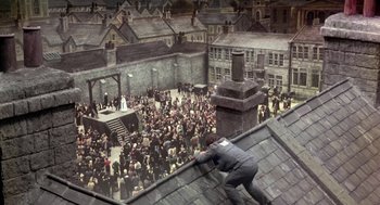 Movie still from “The Great Train Robbery” (1978), directed by Michael Crichton – A man on the roof of a building in front of a crowd of people; Extreme Wide shot, Overhead angle