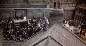 Movie still from “The Great Train Robbery” (1978), directed by Michael Crichton – A man in a gorilla suit jumping off the roof of a building in front of a crowd of onlookers; Extreme Wide shot, Overhead angle