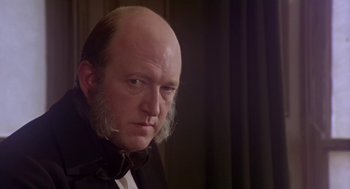 Movie still from “The Great Train Robbery” (1978), directed by Michael Crichton – A man with a beard wearing a black suit and a bow tie; Close Up shot, Over the shoulder angle