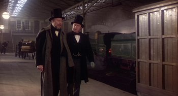 Movie still from “The Great Train Robbery” (1978), directed by Michael Crichton – Two men in top hats and suits walking in front of a train; Medium shot, Over the shoulder angle