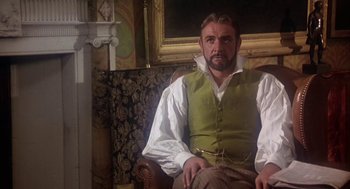 Movie still from “The Great Train Robbery” (1978), directed by Michael Crichton – A man sitting in a chair wearing a green vest; Medium shot, Low angle