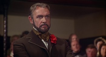Movie still from “The Great Train Robbery” (1978), directed by Michael Crichton – A man with a beard wearing a brown suit and a red flower in his lapel; Close Up shot, Low angle
