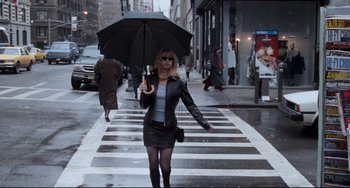 Movie still from “The First Wives Club” (1996), directed by Hugh Wilson – A woman walking across a street holding an umbrella; Wide shot, Low angle