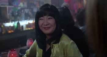Movie still from “The First Wives Club” (1996), directed by Hugh Wilson – A woman in a yellow jacket smiling for the camera; Close Up shot, High angle