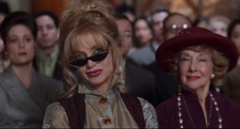 Movie still from “The First Wives Club” (1996), directed by Hugh Wilson – A woman with sunglasses is standing in front of a group of people; Close Up shot, Over the shoulder angle