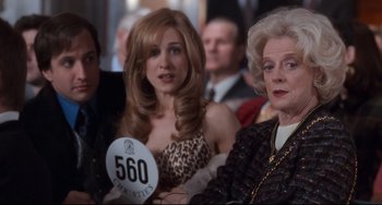 Movie still from “The First Wives Club” (1996), directed by Hugh Wilson – Two women and a man are sitting in front of a group of other people; Close Up shot, Over the shoulder angle