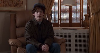 Movie still from “The First Wives Club” (1996), directed by Hugh Wilson – A young man sitting on top of a brown couch; Medium shot, Over the shoulder angle
