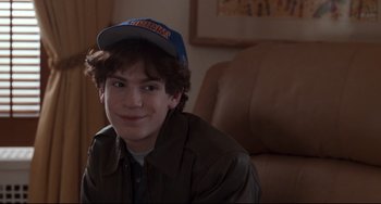 Movie still from “The First Wives Club” (1996), directed by Hugh Wilson – A young man wearing a baseball cap sitting on a couch; Close Up shot, Over the shoulder angle