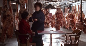 Movie still from “The First Wives Club” (1996), directed by Hugh Wilson – A woman in a red jacket is holding a knife; Medium shot, Over the shoulder angle