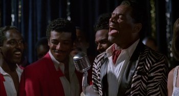 Movie still from “The Five Heartbeats” (1991), directed by Robert Townsend – A group of men standing next to each other with a microphone; Medium shot, High angle