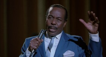 Movie still from “The Five Heartbeats” (1991), directed by Robert Townsend – A man in a blue suit and tie holding a microphone; Close Up shot, High angle