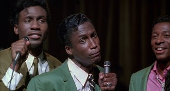 Movie still from “The Five Heartbeats” (1991), directed by Robert Townsend – A man in a green jacket holding a microphone; Close Up shot, High angle