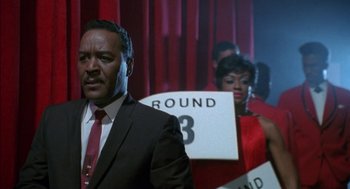 Movie still from “The Five Heartbeats” (1991), directed by Robert Townsend – A man in a suit and tie standing next to a woman in a red dress; Medium shot, High angle