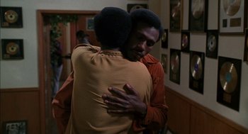 Movie still from “The Five Heartbeats” (1991), directed by Robert Townsend – Two men hugging each other in front of a wall of pictures; Medium shot, Over the shoulder angle