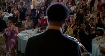 Movie still from “The Five Heartbeats” (1991), directed by Robert Townsend – A man standing in front of a crowd of people at an event; Medium shot, Over the shoulder angle