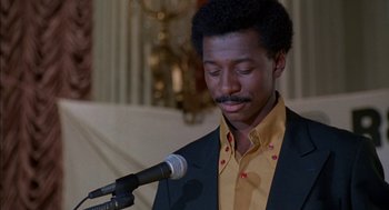 Movie still from “The Five Heartbeats” (1991), directed by Robert Townsend – A man in a yellow shirt is speaking into a microphone; Close Up shot, Low angle