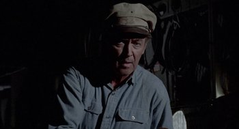 Movie still from “The Flight of the Phoenix” (1965), directed by Robert Aldrich – An older man wearing a hat and a blue shirt; Medium shot, Over the shoulder angle